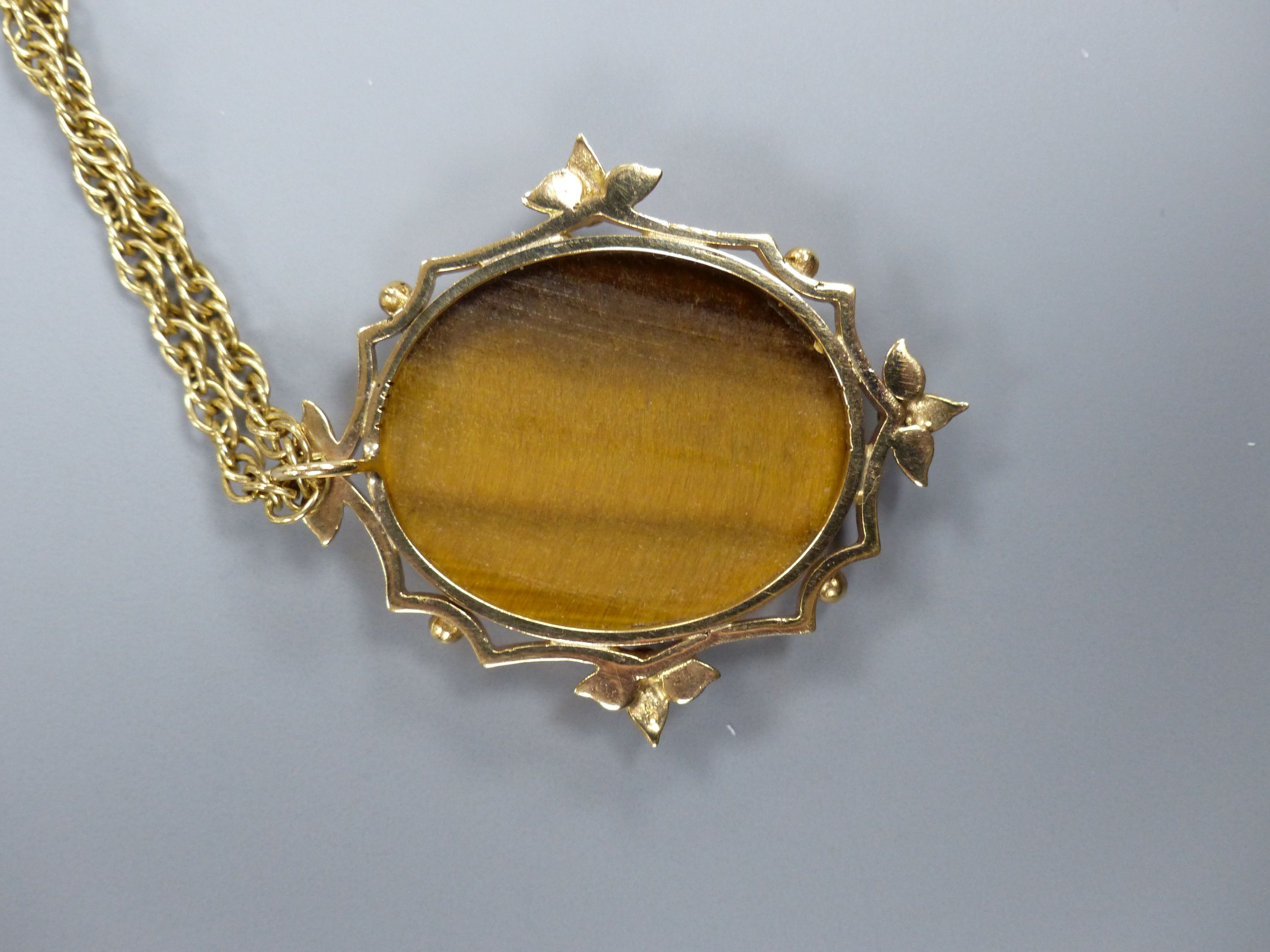 A yellow metal mounted tiger's eye quartz oval pendant, on a 9ct chain